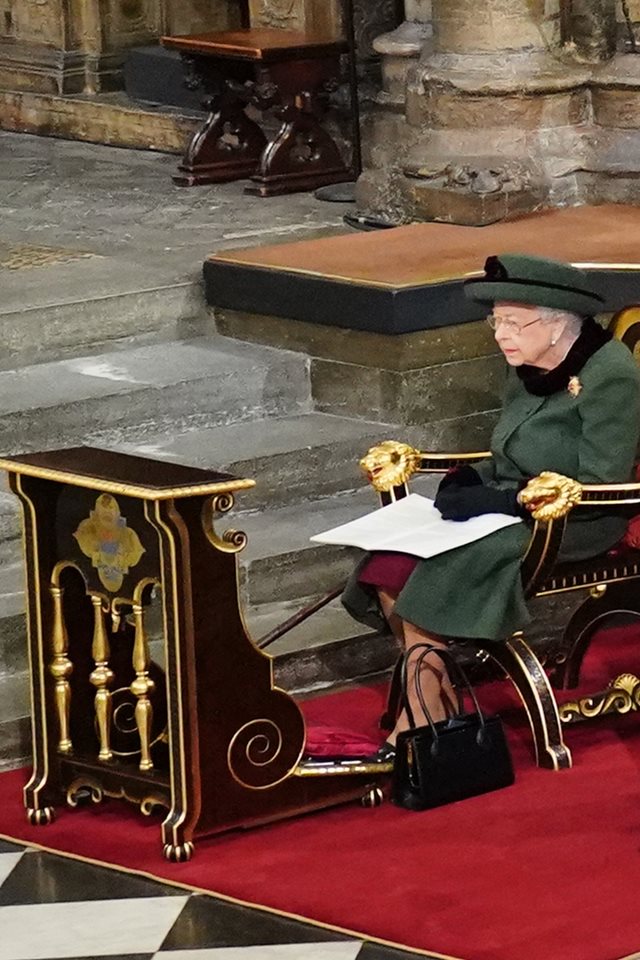 Foto colorida. Rainha Elizabeth sentada em uma cadeira de luxo