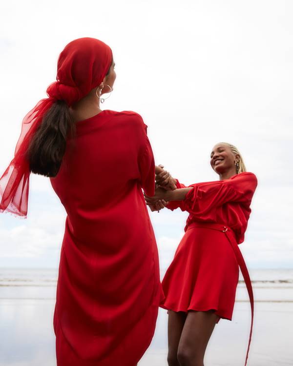 Mulheres usando looks vermelhos e rodando de mãos dadas na praia