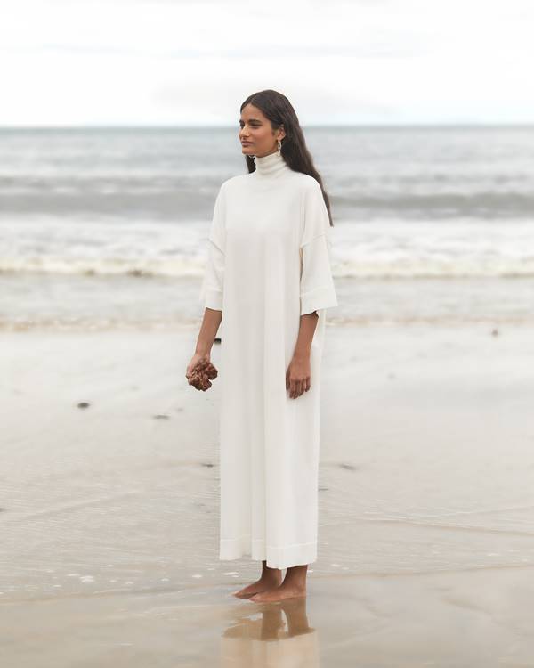 Mulher com vestido branco de gola alta na praia