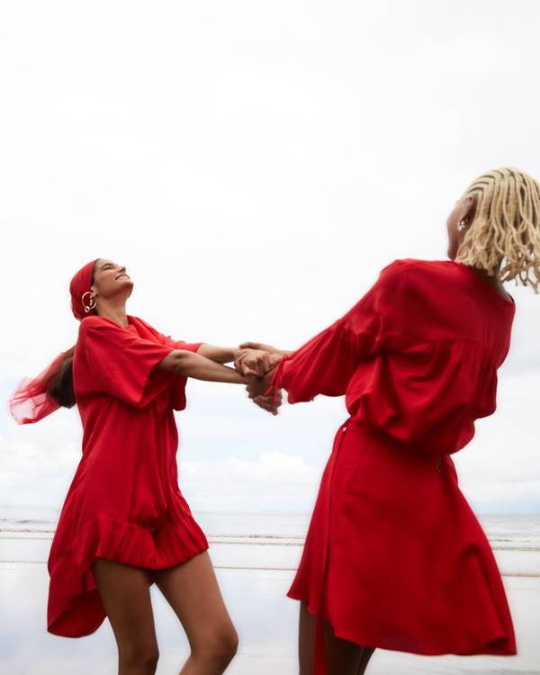 Mulheres usando looks vermelhos e rodando de mãos dadas na praia