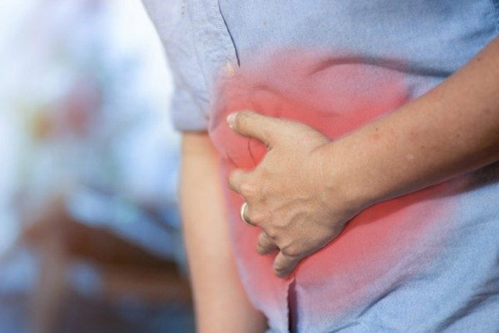 Foto de um homem com dor pressionando com a mão a região do intestino