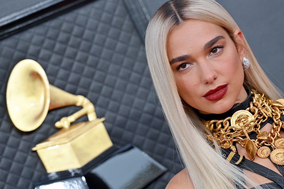 Dua Lipa, no tapete vermelho do Grammy 2022, usando vestido preto colado e longo, com detalhes dourados - Metrópoles