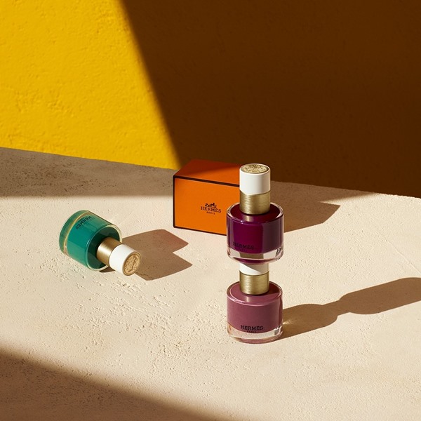 Esmaltes da Hermès e caixa da mesma marca. Dois dos produtos são em um tom de vinho e o terceiro esmalte é verde.