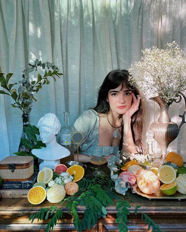 Mulher posa em frente a um arranjo de flores com a mão no queixo