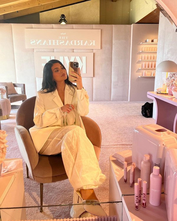 Kylie Jenner com look todo branco e bolsa transparente da marca francesa Coperni. Ela está sentada em uma cadeira rosa no camarim