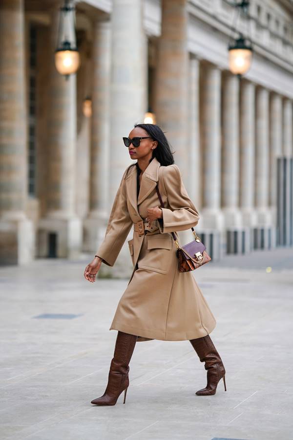 Mulher negra usando trench coat com ombreiras e bota marrom over the knee