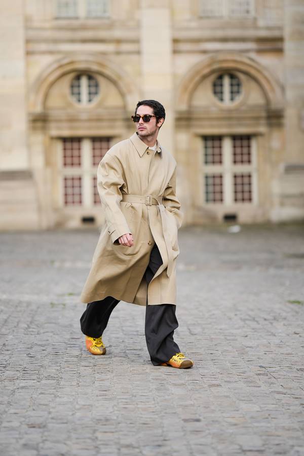 Homem branco usando trench coat bege com calça escura e tênis amarelo