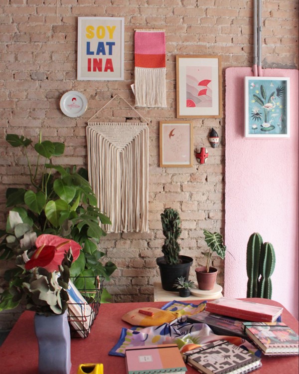 Parede de tijolimnho com vários quadros e objetos de decoração. Na foto também é possível ver uma mesa e vasos com plantas.