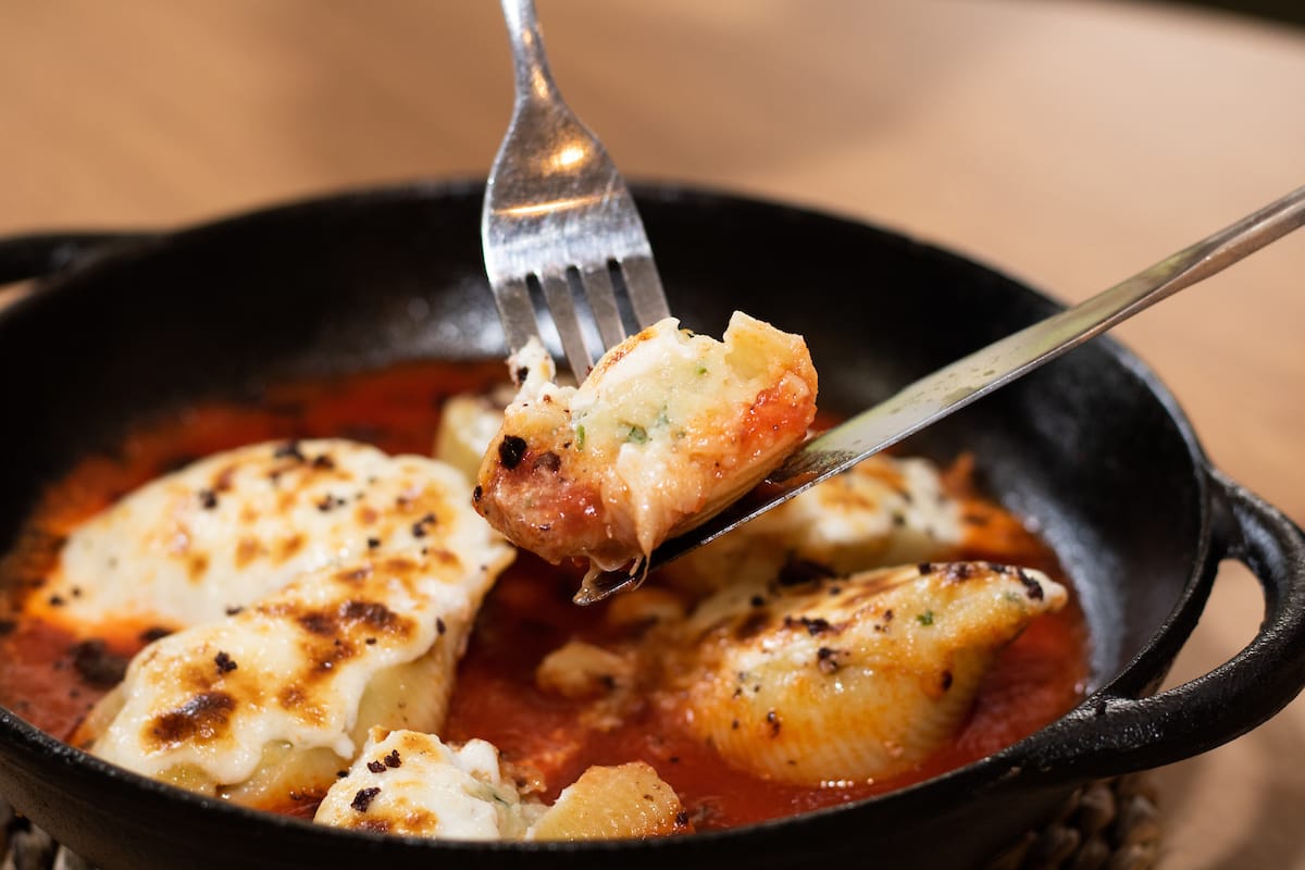 na foto vemos uma panelinha preta com massa recheada de bacalhau e molho de tomate