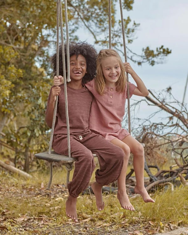 Uma menina negra com cabelo black power e outra branca e loura brincando em balanço em um jardim