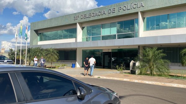 Foto de homem acompanhado de um policia na entrada da 38ª Delegacia da Polícia