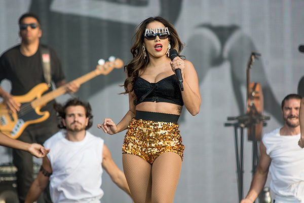 Anitta em show no Rock in Rio de Lisboa, em 2019. Ela usa um óculos com letras brilhosas que formam seu nome, um top preto e um short de lantejoulas douradas