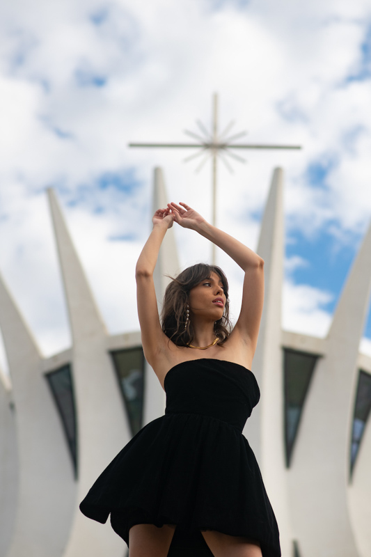 Modelo de cabelo médio e franja usa vestido preto com volume e coturno