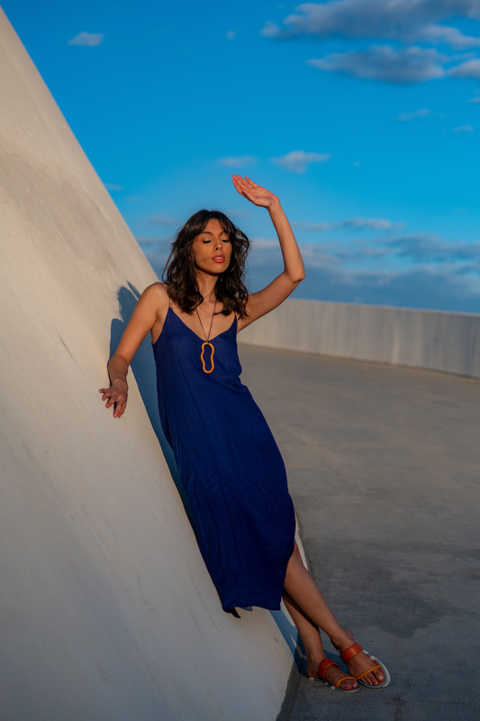 Modelo de cabelo médio e franja usa vestido azul fluido com colar geométrico