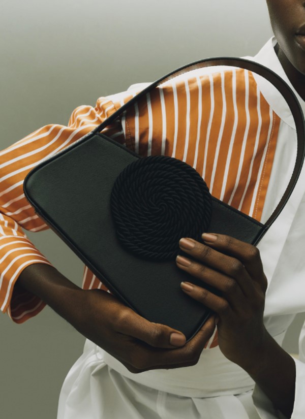 Mulher negra segurando bolsa preta com alça curta e um detalhe redondo de corda