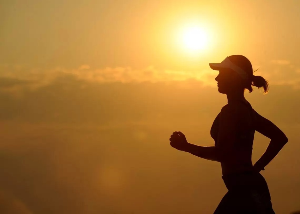 mulher corre ao ar livre e é fotografada com o pôr do sol ao fundo