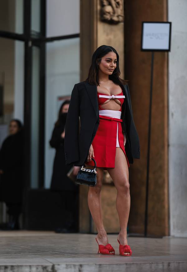 Vanessa Hudgens usando top e minissaia com fenda vermelhos, e blazer escuro nos ombros