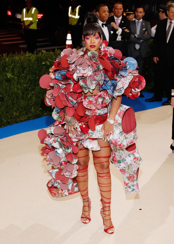 Rihanna no tapete vermelho do Met Gala de 2016. Ela usa um vestido cheio de retalhos, nas cores vermelho, azul, branco e rosa. Usa, ainda, uma sandália de tira vermelha que amarra acima do joelho. 