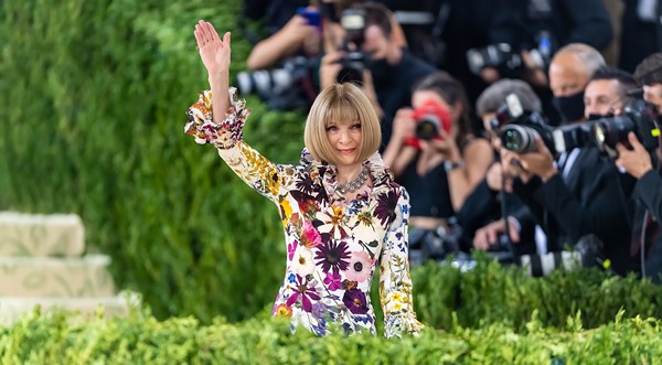 Mulher branca, com cabelo curto e louro, e roupas estampadas. Ela está no tapete vermelho do Met Gala. Seu nome é Anna Wintour.