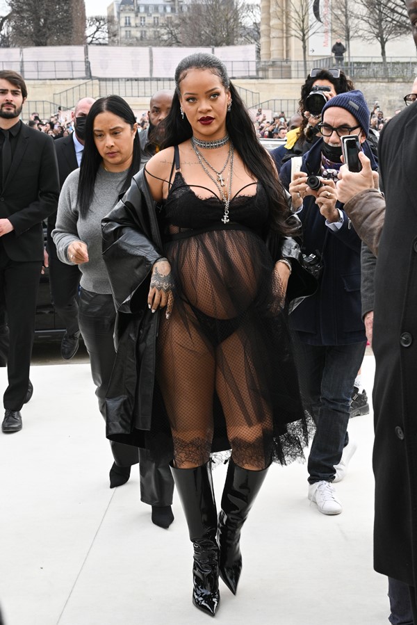 Cantora Rihanna na entrada do desfile da Dior. Ela está grávida e usa uma lingerie preta e um vestido de renda transparente por cima.