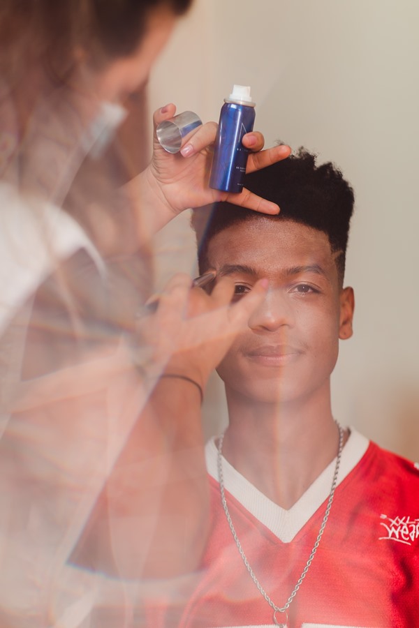 Homem negro, com cabelo black, sendo maquiado por uma mulher para uma competição. O modelo participou do concurso de beleza Top Cufa DF