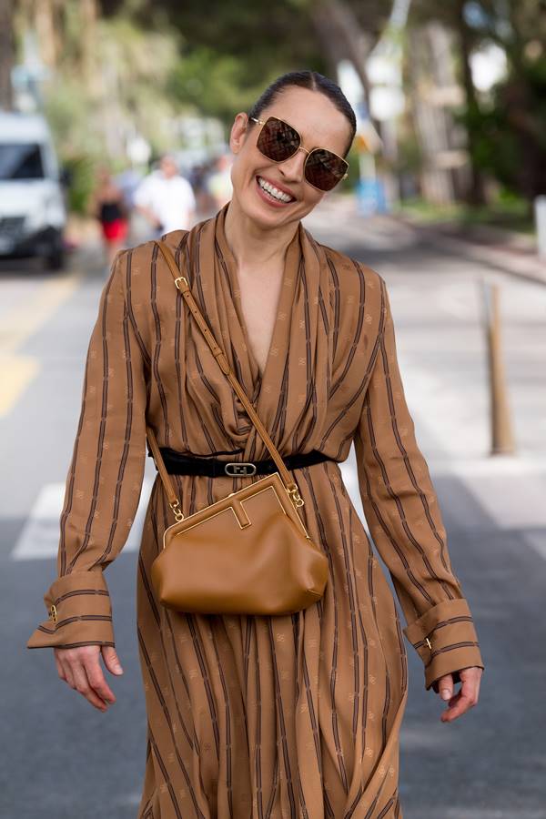 Mulher branca andando na rua com uma bolsa de couro marrom