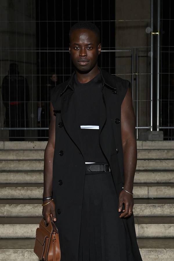 Homem negro usa colete preto, blusa preta e calça preta 