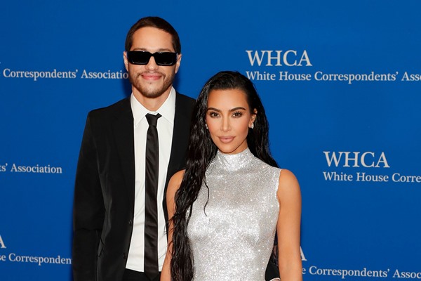 Empresária Kim Kardashian e o namorado, o comediante Pete Davidson, na entrada de um evento da Casa Branca norte-americana. Ele usa um terno clássico preto, com camisa branca e gravata também preta. Kim usa um vestido rente ao corpo, prateado, com o cabelo preto solto e ondulado.