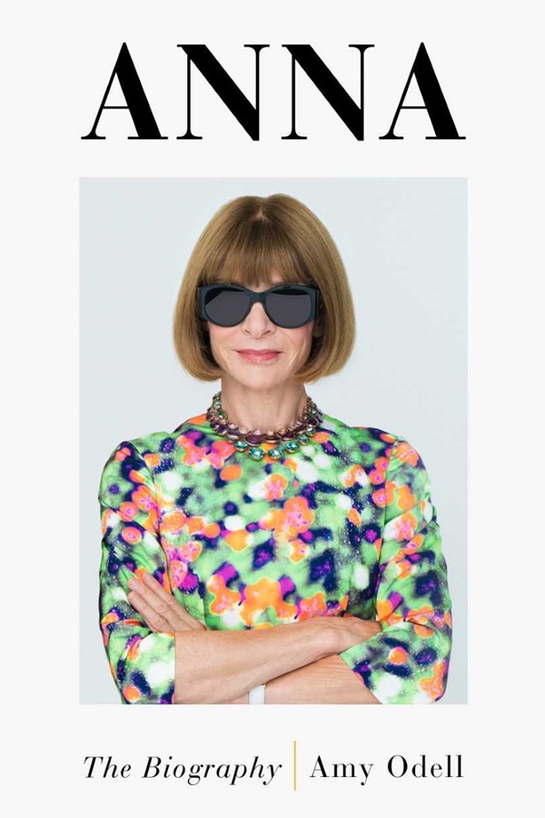 Capa do livro que conta a biografia da jornalista de moda e chefe da Vogue, Anna Wintour. A capa do livro é branca com escritos em preto, em uma fonte com serifa, e no centro, está a foto da jornalista. Ela é uma mulher idosa branca, com cabelos curtos e franja na cor louro médio. Usa um óculos escurtos e um vestido colorido.