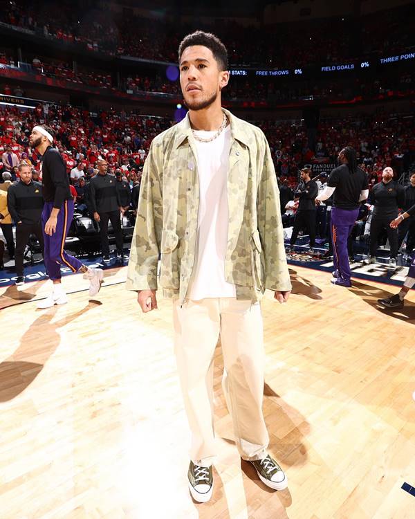 Jogador de basquete no meio da quadra depois do jogo usa camisa branca, jaqueta verde com estampas suaves e all star nos pés