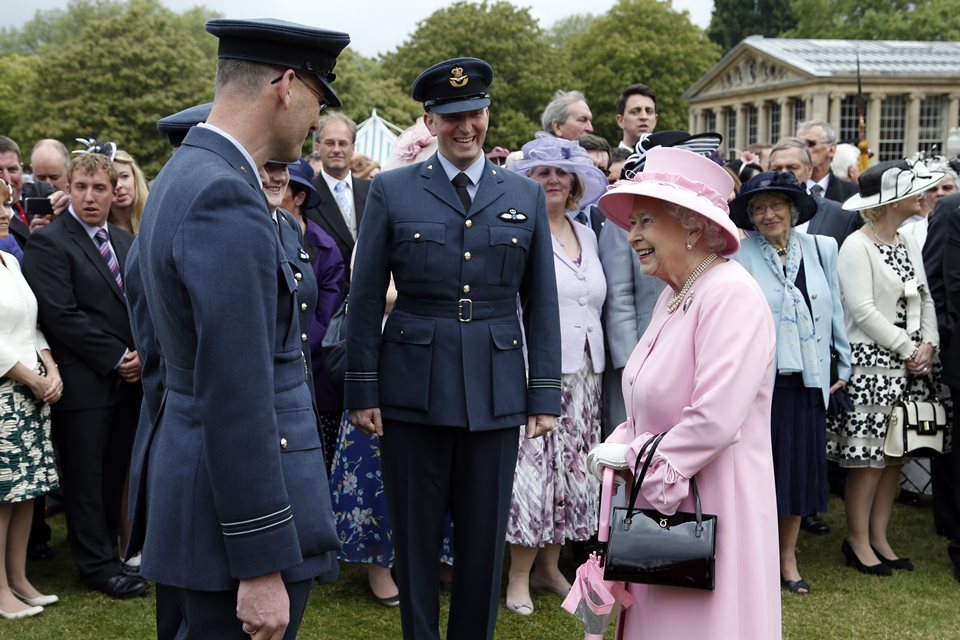 Foto colorida. Rainha Elizabeth ao lado de militares