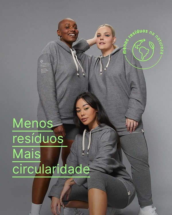 Campanha de divulgação dos moletons da marca Malwee, feitos a partir de um fio reciclado. Posam para foto, com o mesmo conjunto de calça e moletom cinza, três modelos: uma mulher negra com cabelo raspado; uma asiática com cabelo preto e liso; e uma branca com cabelo louro descolorido.