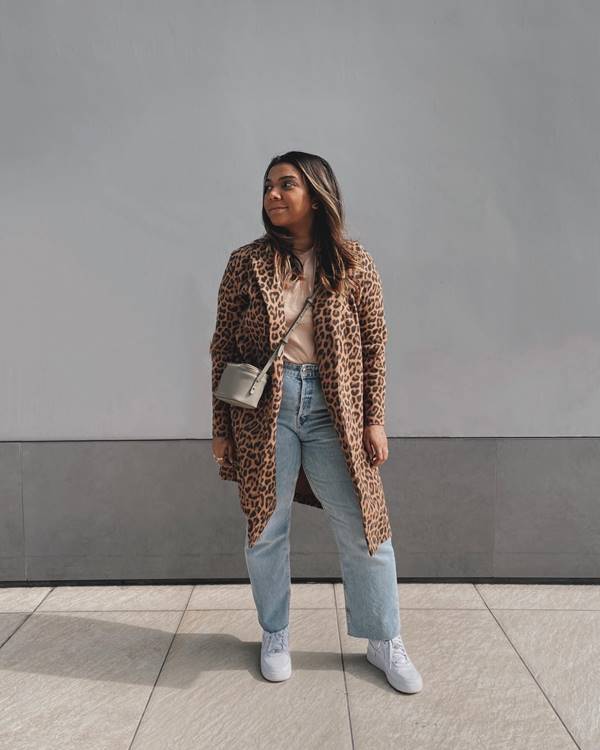 mulher de cabelo solto usa casaco com estampa de onça, calça jeans e bolsa cinza