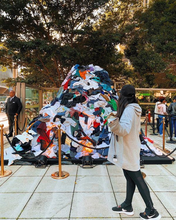 Meninas branca, com cabelo castanho, andando pela rua em frente a uma pilha de roupas descartadas