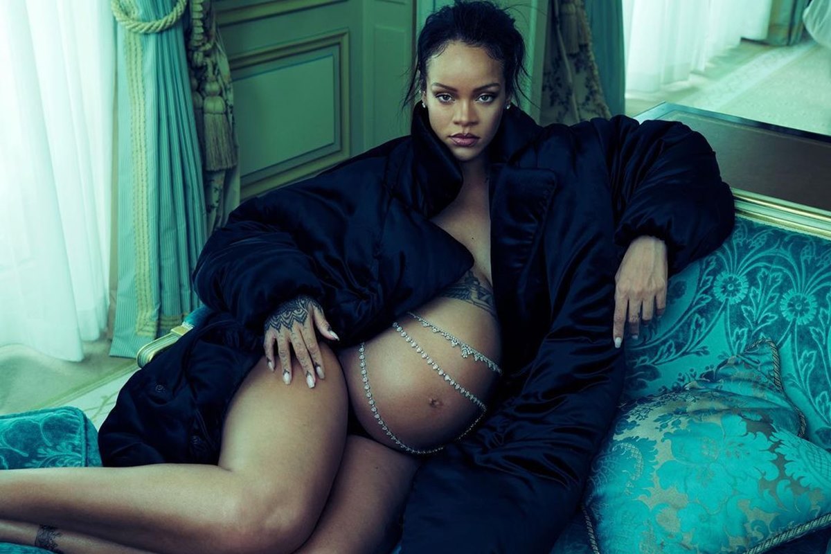 rihanna deitada de lado em sofá com barriga de gravida a mostra e um sobretudo