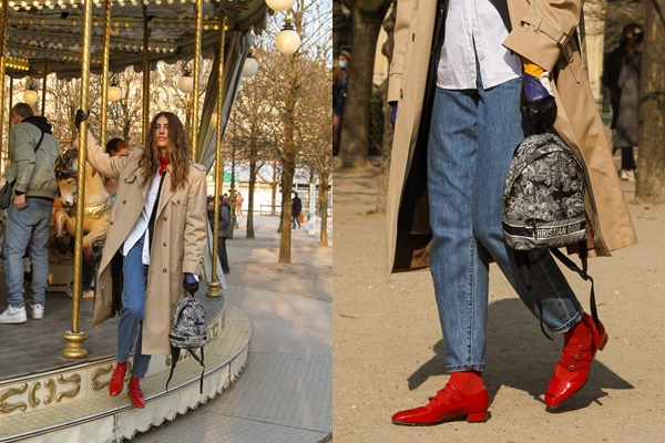 Mulher branca, com cabelo ondulado castanho claro, posando para foto em um carrossel nas ruas de Paris, na França. Ela usa uma camise branca de botão, um sobretudo bege, calça jeans, meia-calça vermelha e uma sandália de bico redondo também vermelha.