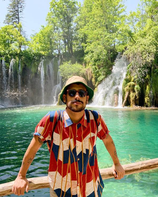 Homem branco usa camisa estampada com bucket hat e óculos de sol