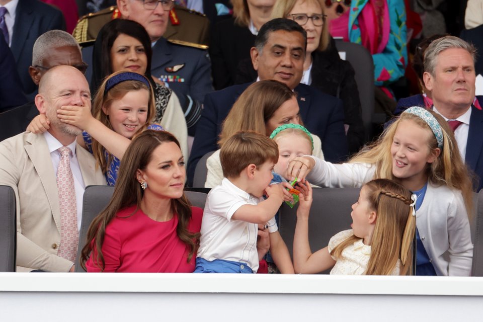 Foto colorida. Mia Grace tampa a boca do pai, Mike Tindall, enquanto Charlotte e Louis dividem guloseimas com Lena e Savannah