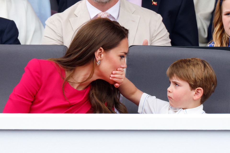 Foto colorida. Menino tampa a boca de mulher de vestido vermelho - Metrópoles