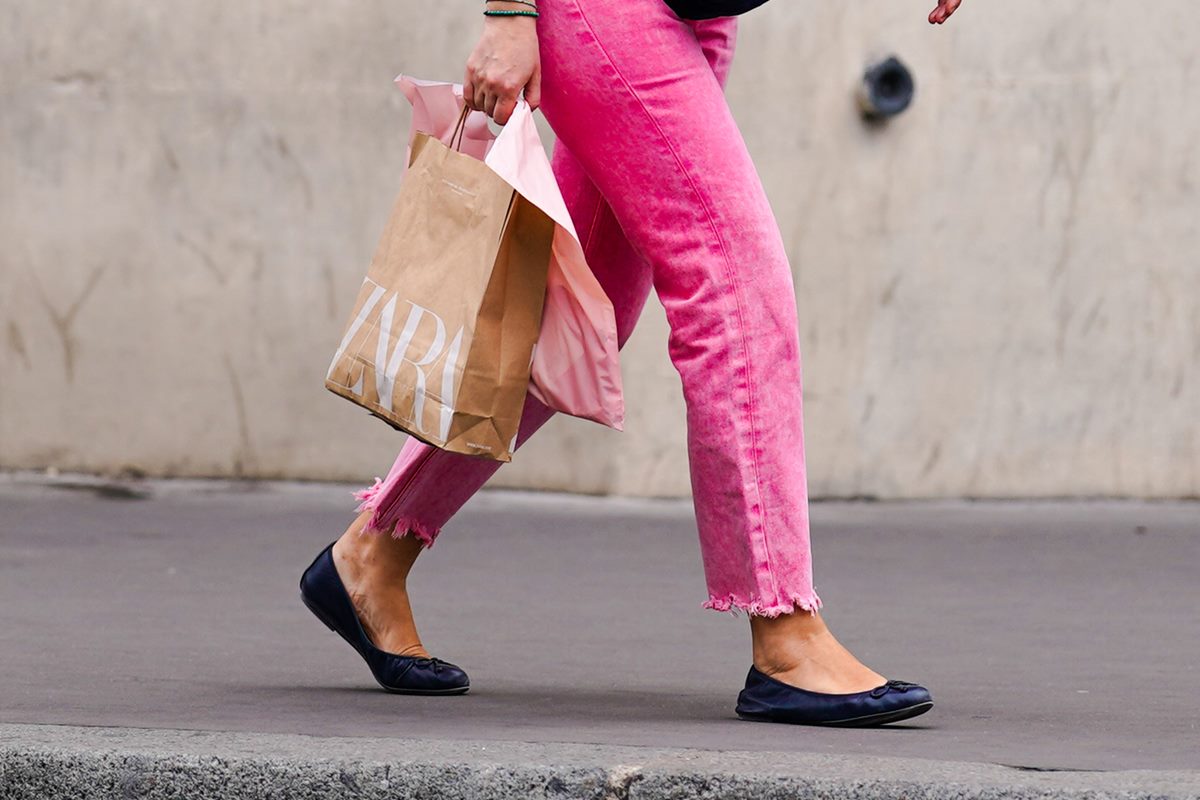 mulher branca com calça rosa segurando sacola de papel