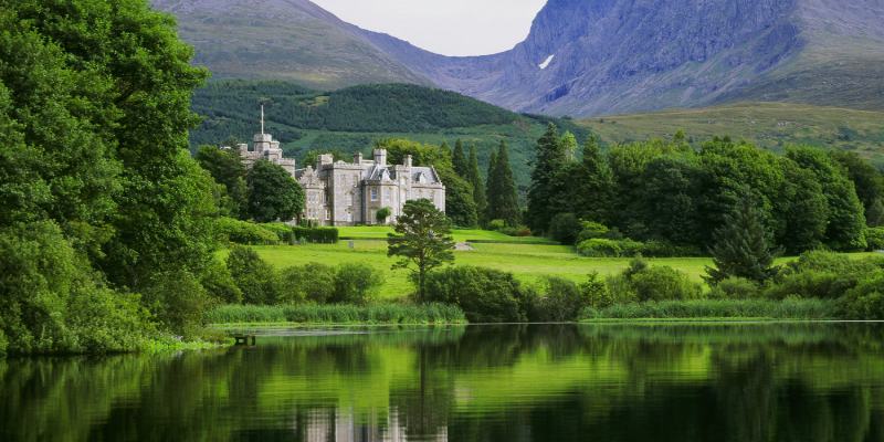 fotografia colorida de imagem de castelo com montanhas atrás e lago na frente