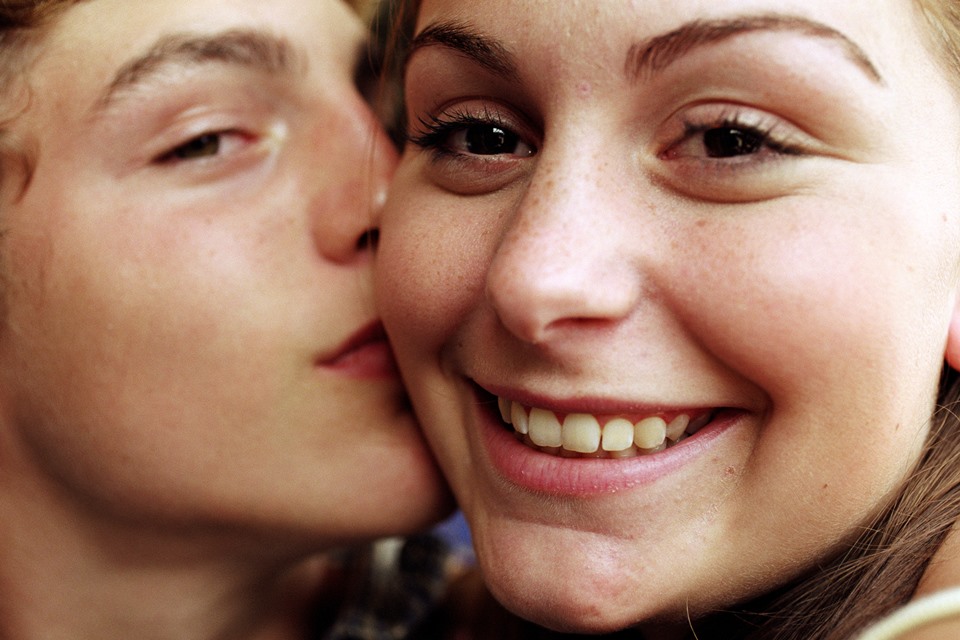 Foto colorida. Casal beijando na bochecha