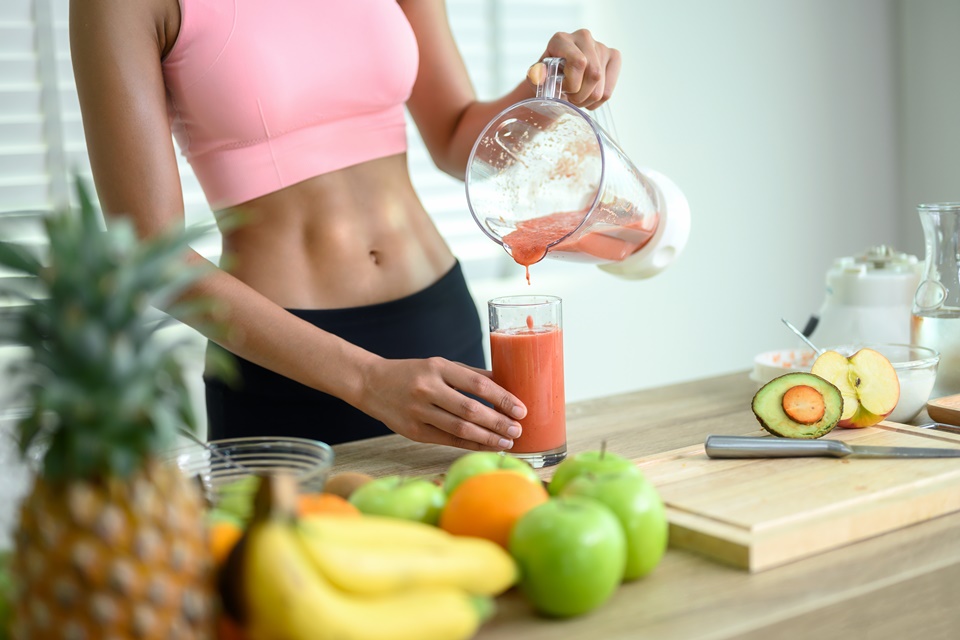 Foto colorida. Mulher com a barriga à mostra. Ela segura um liquidificador