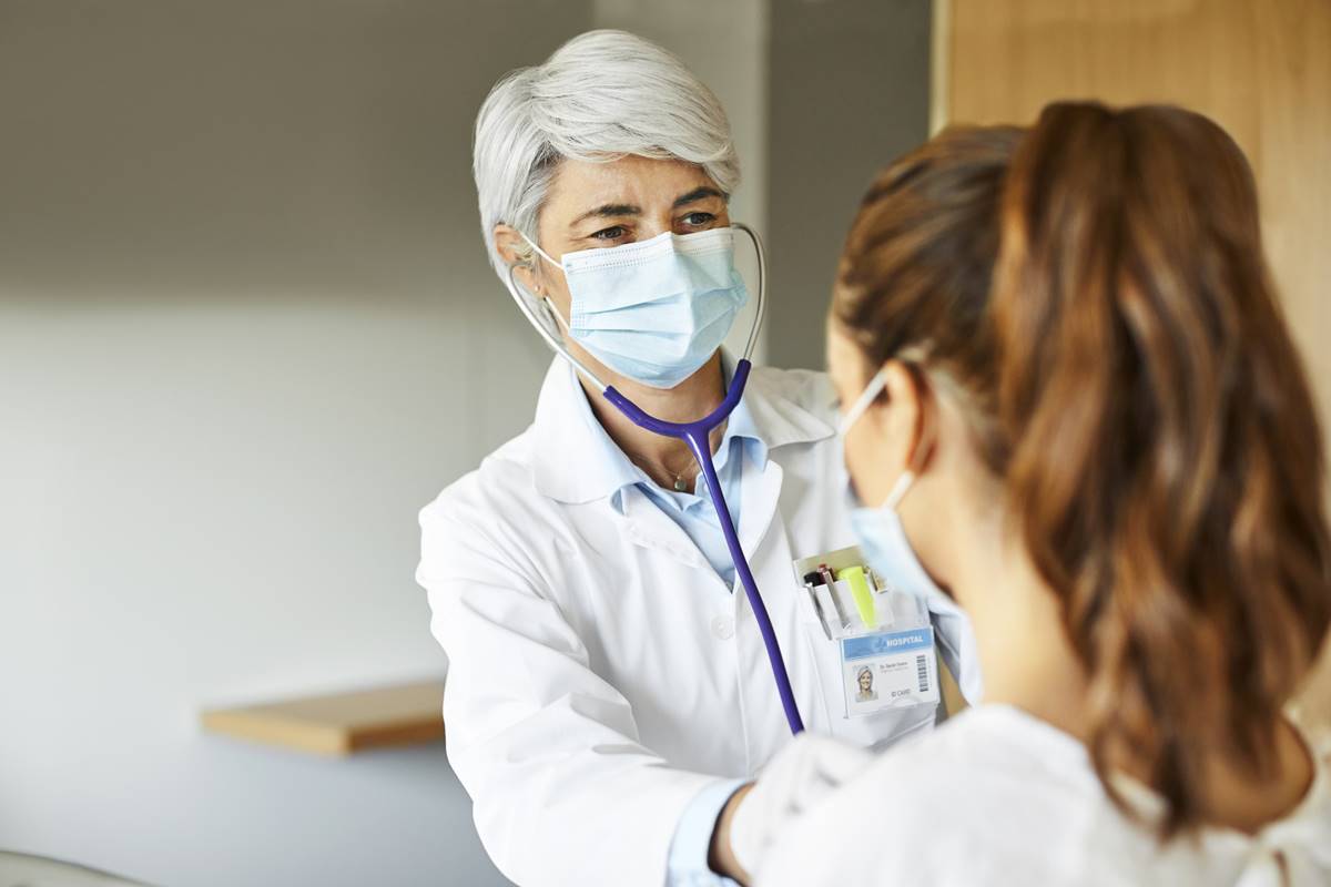 Foto de uma médica examinando uma moça jovem com o cabelo amarrado