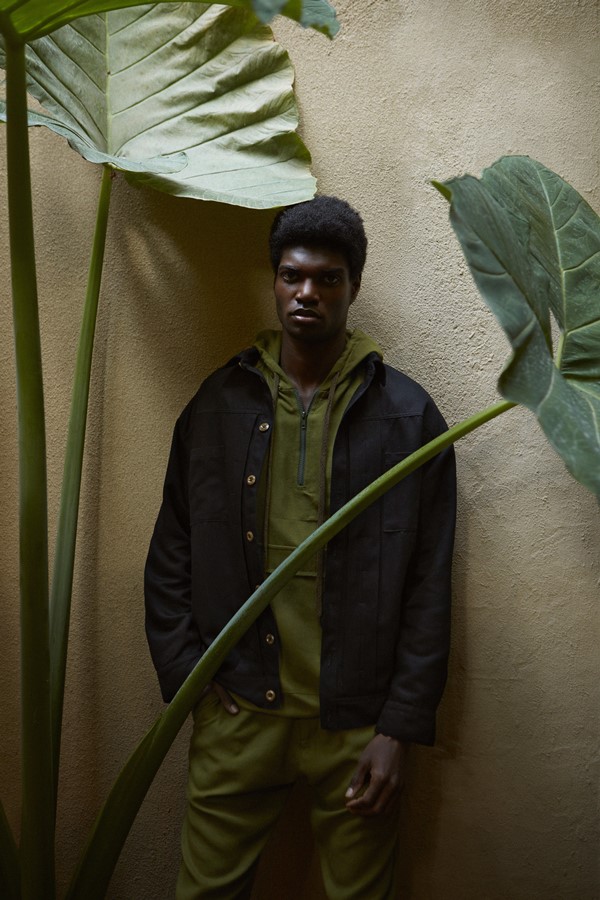 Foto de divulgação da nova coleção de roupas da marca Dafiti. Na foto, modelo posa com itens da etiqueta. É um homem jovem, negro, com cabelo curto, que veste casaco de moletom e calça de moletom em tom de verde militar e, por cima, uma parka preta.