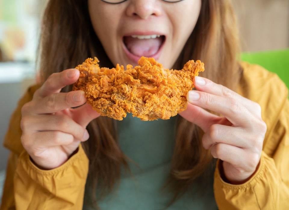 Foto colorida de mulher comendo alimento empanado e frito com as mãos - Metrópoles