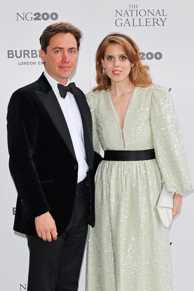 Foto colorida. Homem branco vestido de terno ao lado de mulher branca ruiva com um vestido branco