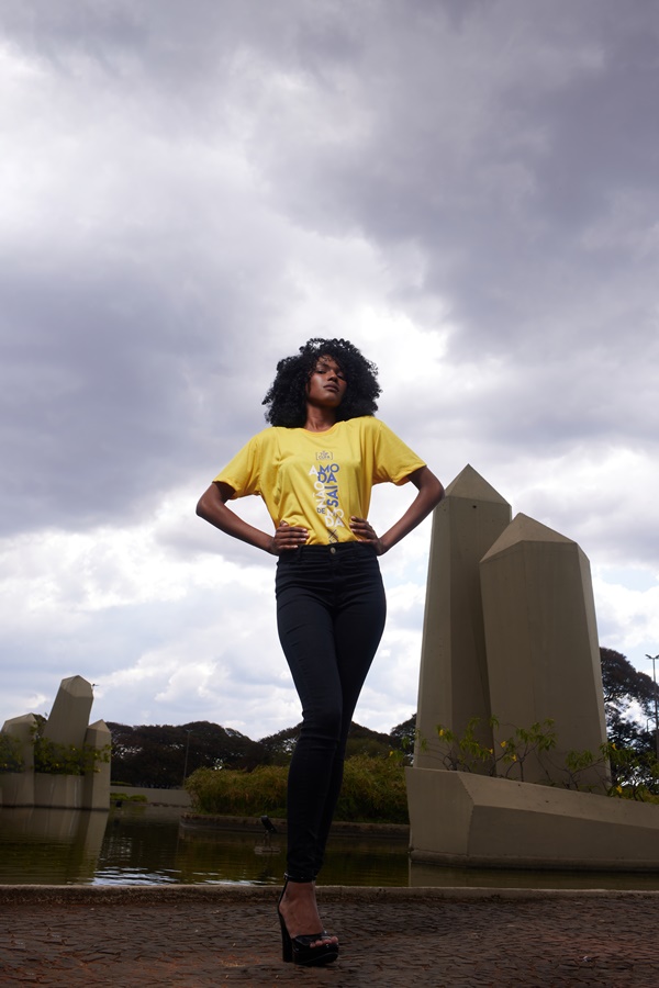 Gabriella Santana, vencedora do concurso Top Cufa DF 2022, uma menina jovem negra com cabelo cacheado posando para foto de calça jeans e camiseta amarela