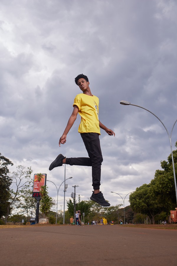 Rhuan Fara=ia, vencedor do concurso Top Cufa DF 2022, um menino jovem negro com cabelo cacheado posando para foto de calça jeans e camiseta amarela