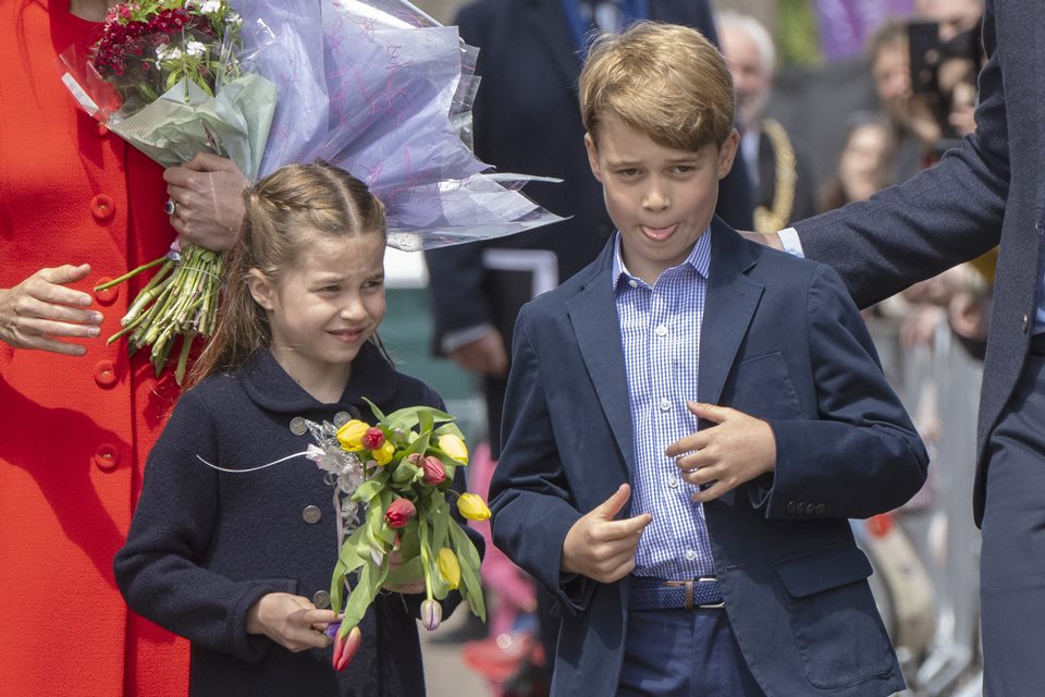 Foto colorida. Menina branca segura um buquê e menino branco pega no blazer